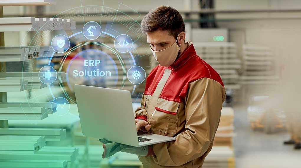 Worker using a laptop with ERP solution icons in a factory